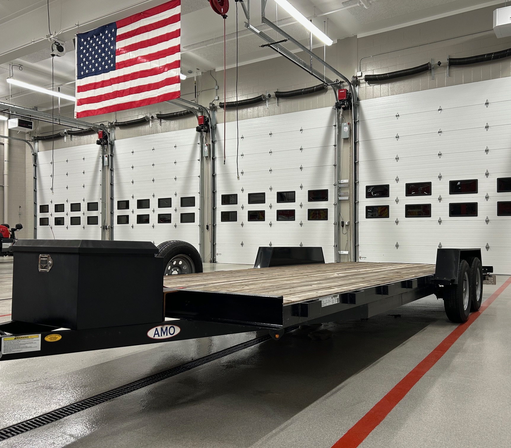 True Rentals professional garage facility in Rockford, Michigan with AMO flatbed car hauler trailer and American flag